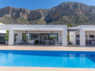 La moderna villa presenta una piscina azul brillante, terraza cubierta con salón y comedor exterior, además de cocina integrada al aire libre, con vistas al Montgó.