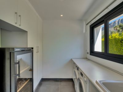 Lavadero moderno con lavadora, secadora y vinoteca integradas, complementado con gabinetes blancos y vistas a la montaña desde la ventana.