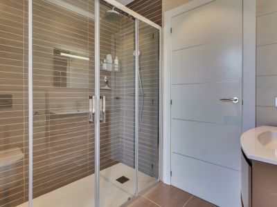 Moderno cuarto de baño con amplia ducha acristalada, cabezal de lluvia y azulejos taupe con rayas horizontales. Incluye inodoro suspendido y lavabo con mueble contemporáneo.
