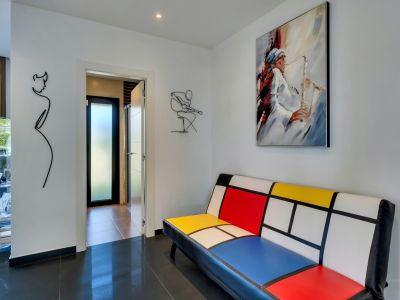 Pasillo moderno con sofá de diseño Mondrian, cuadro de saxofonista y arte de alambre minimalista, sobre suelo de baldosas oscuras y brillantes.