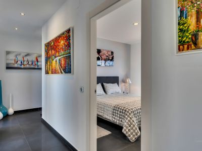Pasillo moderno con suelo de gres oscuro, iluminación empotrada y vibrante arte abstracto, que conduce a un dormitorio con cama estampada y lámpara de noche.