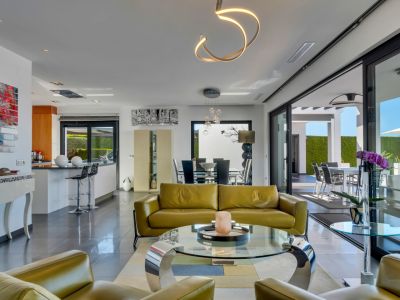 Salón de planta abierta con sofás de piel verde oliva, mesa de centro de cristal y acceso directo a la terraza exterior mediante grandes puertas correderas. Iluminación moderna.