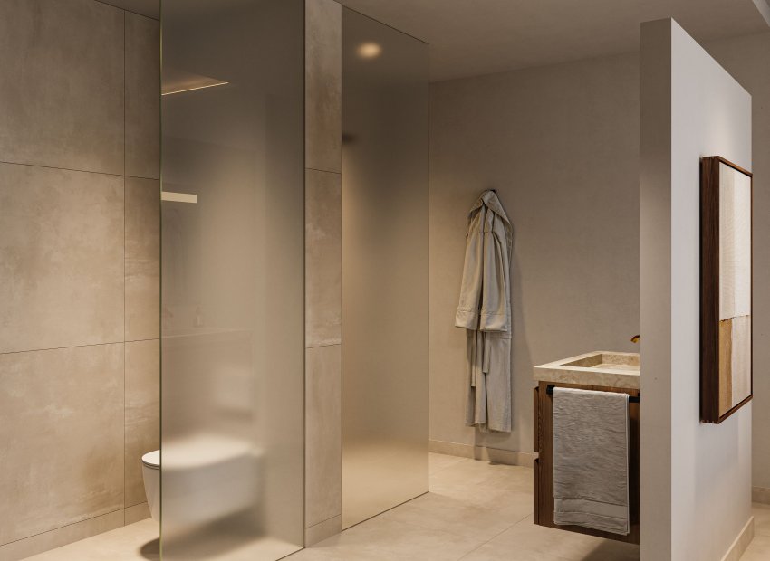 Baño moderno con mampara de cristal esmerilado para el inodoro, lavabo de piedra sobre un mueble de madera oscura y azulejos de gran formato en tonos neutros. Iluminación empotrada realza el diseño minimalista.