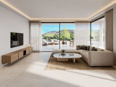 Amplio salón con sofá esquinero neutro, mesa de centro ovalada y mueble flotante de madera. Grandes puertas correderas de cristal conectan con una espaciosa terraza y vistas panorámicas a las colinas verdes.