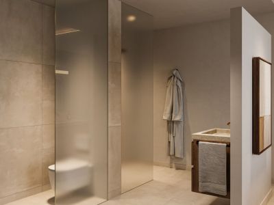 Baño moderno con mampara de cristal esmerilado para el inodoro, lavabo de piedra sobre un mueble de madera oscura y azulejos de gran formato en tonos neutros. Iluminación empotrada realza el diseño minimalista.