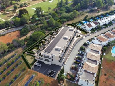 Vista aérea de un edificio moderno con techo solar y una amplia terraza ajardinada con pérgolas, asientos al aire libre y un putting green, junto a un campo de golf.