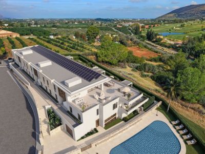 Vista aérea de una residencia de lujo moderna con paneles solares en el tejado, múltiples terrazas exteriores con zonas de estar y comedor, y una gran piscina, enmarcada por un campo de golf y huertos.