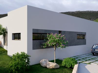 Exterior de villa moderna con fachada blanca y detalles en paneles de piedra oscura. Jardín con césped, árboles y entrada adoquinada con césped, en un entorno montañoso.