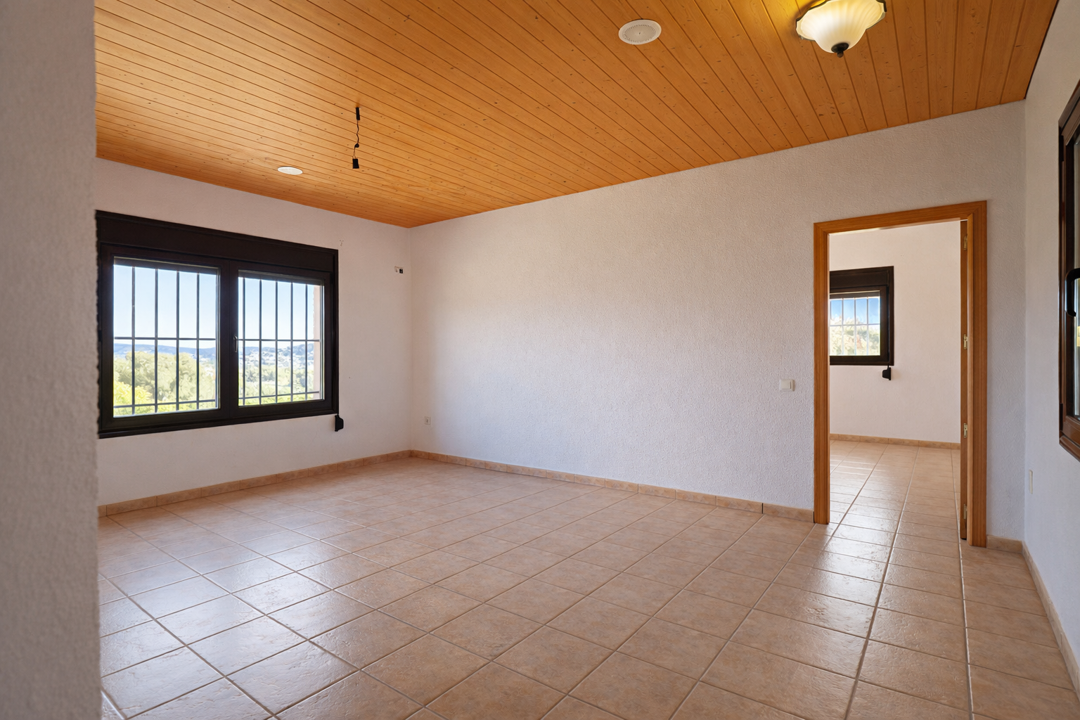 Amplia estancia con suelo de baldosas claras, paredes blancas y techo de madera. Las ventanas con rejas ofrecen vistas panorámicas al valle y abundante luz natural. Amplia estancia con suelo de baldosas claras, paredes blancas y techo de madera. Las ventanas con rejas ofrecen vistas panorámicas al valle y abundante luz natural.