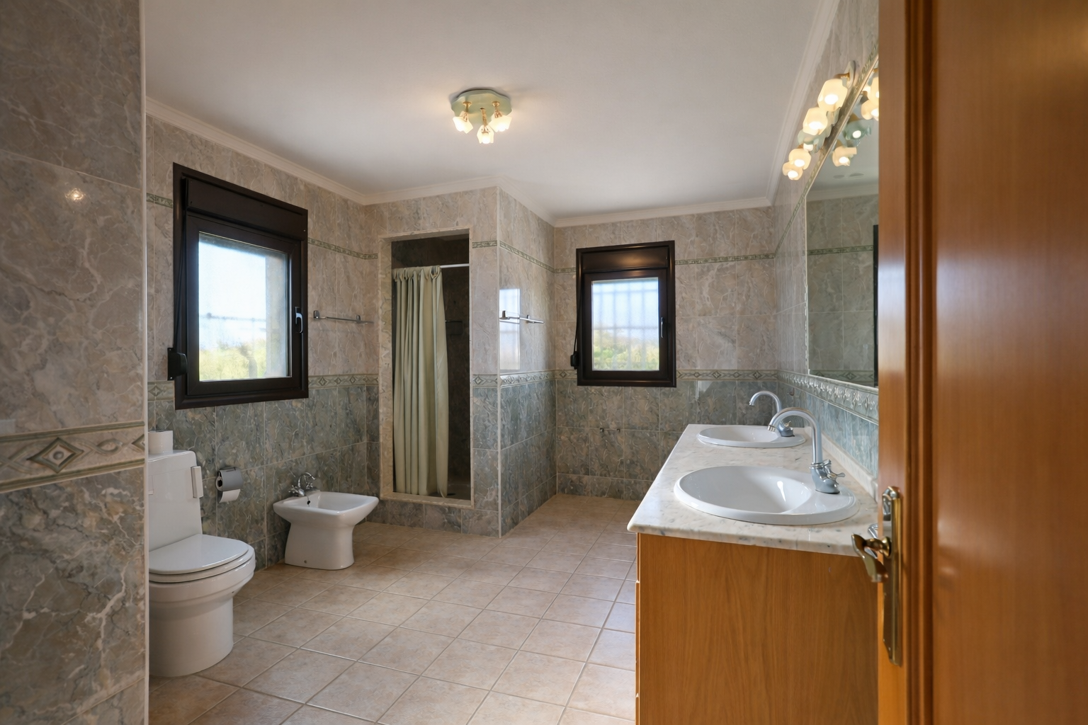 Amplio baño con doble lavabo sobre encimera de mármol y mueble de madera. Cuenta con ducha, inodoro y bidé, paredes alicatadas en tonos grises y verdes, y dos ventanas que aportan luz natural. Amplio baño con doble lavabo sobre encimera de mármol y mueble de madera. Cuenta con ducha, inodoro y bidé, paredes alicatadas en tonos grises y verdes, y dos ventanas que aportan luz natural.