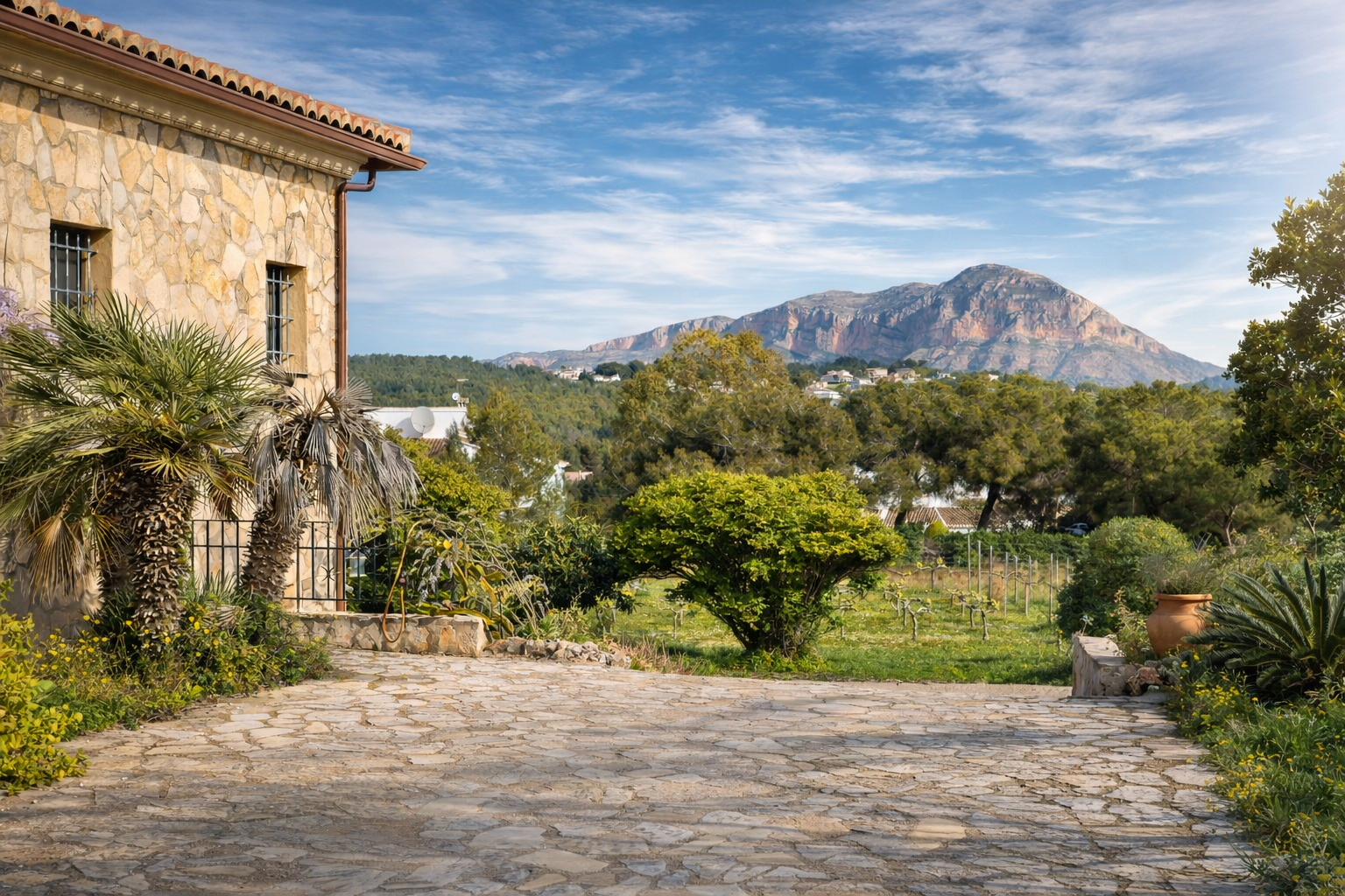 Fachada de piedra rústica de la finca con palmeras, camino de adoquines y vistas al Montgó, rodeada de viñedos y vegetación mediterránea. Fachada de piedra rústica de la finca con palmeras, camino de adoquines y vistas al Montgó, rodeada de viñedos y vegetación mediterránea.