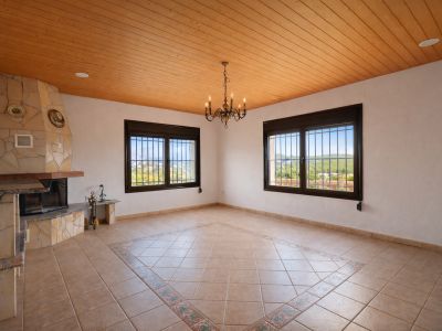 Amplia estancia con chimenea de piedra, techo de madera machihembrada y suelo de baldosas con patrón central decorativo. Dos ventanas enrejadas ofrecen vistas al valle.