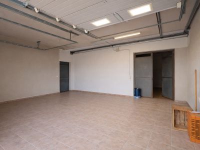 Amplio garaje o sala de servicio con suelo de baldosas claras, techo con luminarias industriales y múltiples accesos.