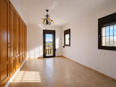 Habitación luminosa con armarios empotrados de madera, suelo de baldosas claras y paredes texturizadas. Dispone de acceso a balcón con vistas al paisaje y ventanas con rejas.