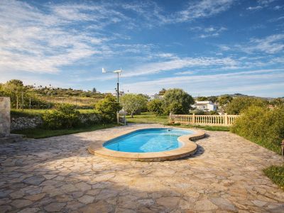 Piscina de forma orgánica rodeada por una amplia terraza de losas irregulares. Al fondo, se aprecian colinas verdes con vegetación y una turbina eólica.