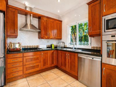 Cocina funcional con armarios de madera cálida, encimeras de granito oscuro y electrodomésticos de acero inoxidable integrados. Ventana con reja decorativa y vistas al exterior.