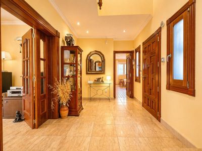 Luminoso pasillo con paredes amarillas cálidas y suelo de baldosas claras. Destacan las puertas de madera oscura, una vitrina decorativa y una consola con espejo arqueado.