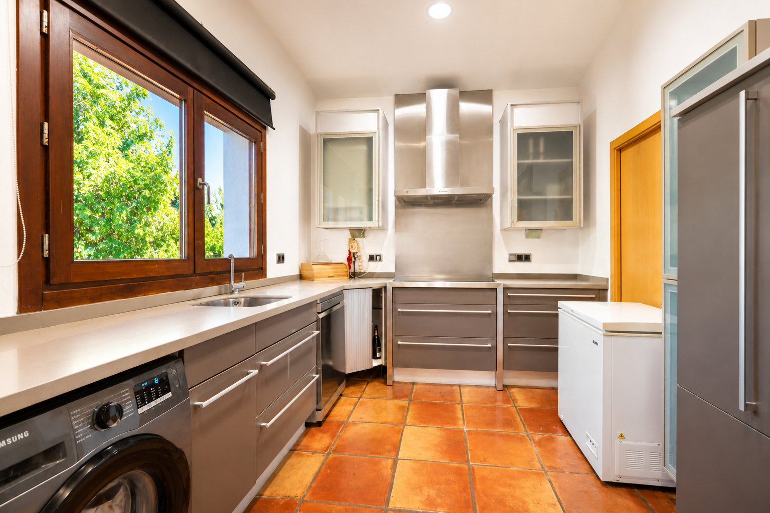 Cocina funcional con lavadora integrada, suelo de barro artesanal y gran ventanal de madera con vistas al jardín. Cocina funcional con lavadora integrada, suelo de barro artesanal y gran ventanal de madera con vistas al jardín.