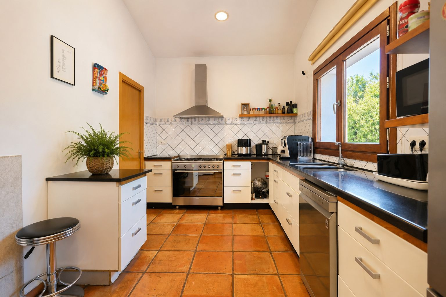 Cocina funcional con suelos de barro artesanal, encimeras oscuras y amplios ventanales de madera que aportan abundante luz natural. Cocina funcional con suelos de barro artesanal, encimeras oscuras y amplios ventanales de madera que aportan abundante luz natural.