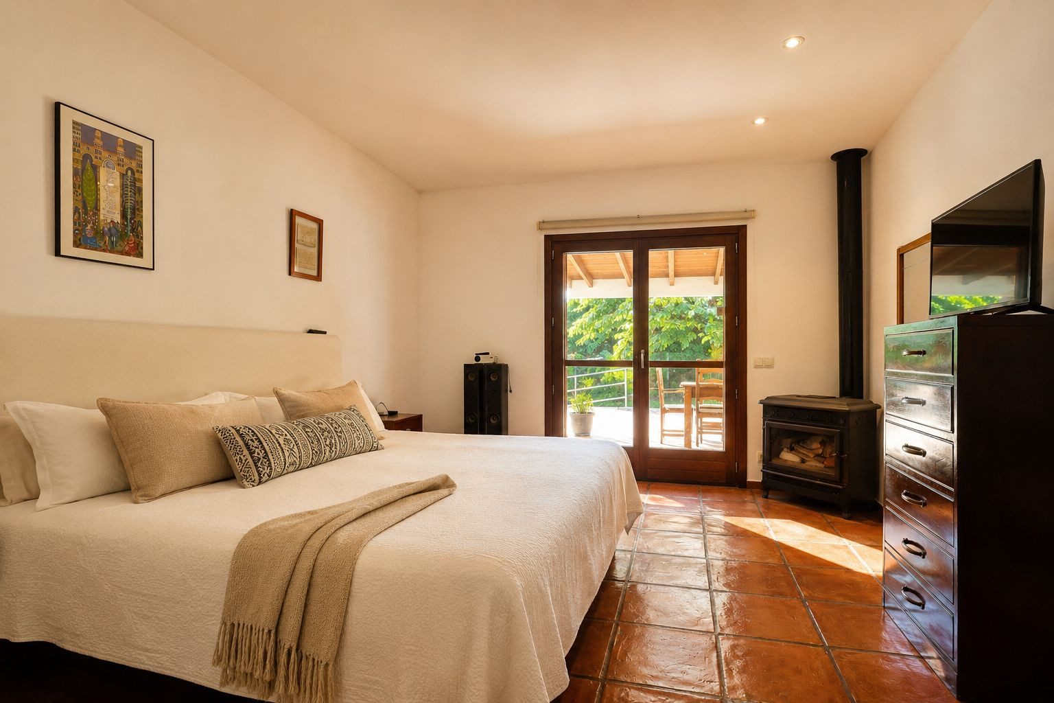 Dormitorio luminoso con cama grande, suelos de barro artesanal y una estufa de leña. La puerta de cristal doble ofrece acceso directo a una terraza exterior rodeada de vegetación. Dormitorio luminoso con cama grande, suelos de barro artesanal y una estufa de leña. La puerta de cristal doble ofrece acceso directo a una terraza exterior rodeada de vegetación.
