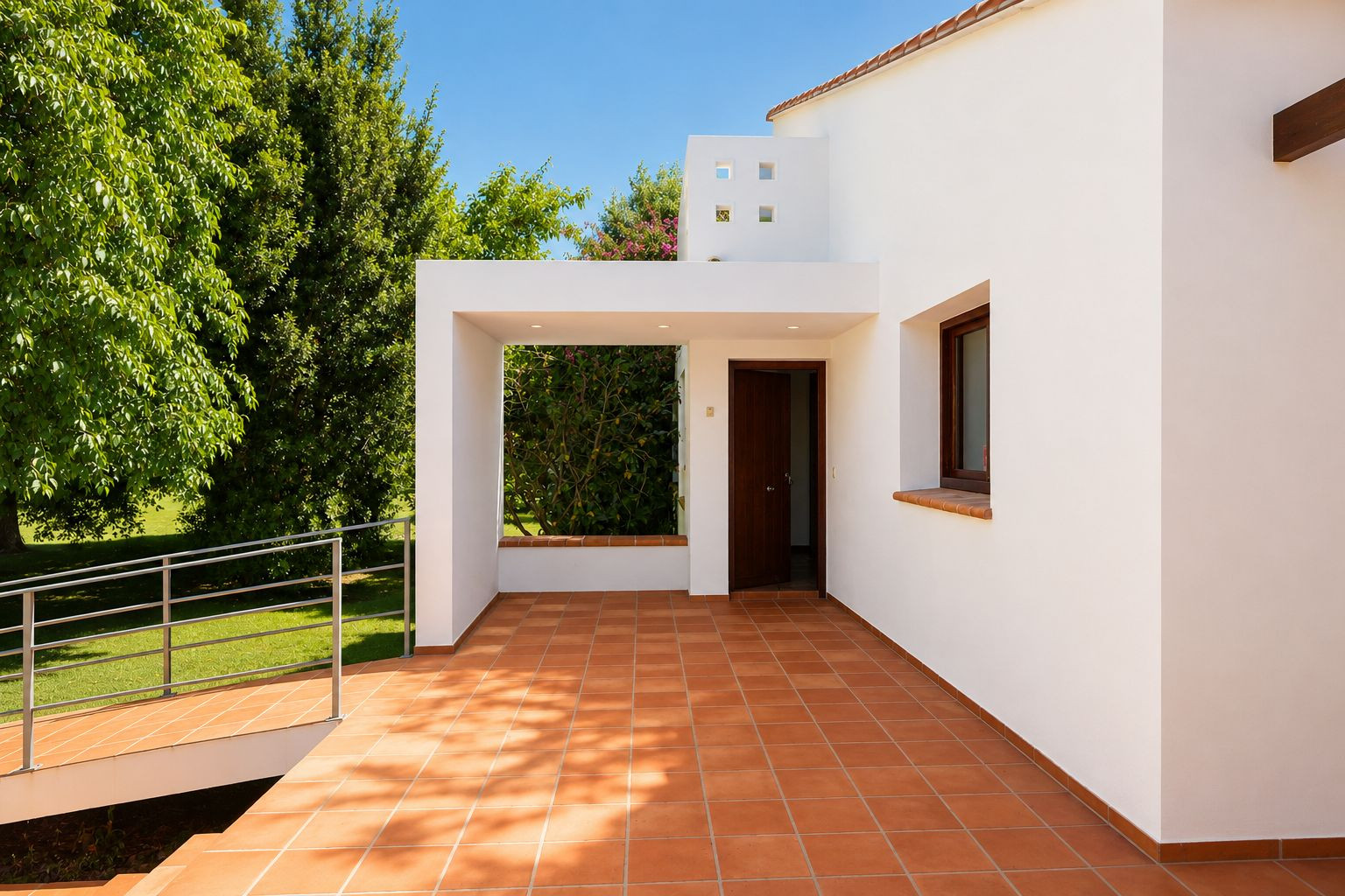 Entrada principal con porche cubierto y suelo de barro artesanal, conectando con una rampa accesible al jardín. La puerta de madera oscura contrasta con las paredes blancas. Entrada principal con porche cubierto y suelo de barro artesanal, conectando con una rampa accesible al jardín. La puerta de madera oscura contrasta con las paredes blancas.