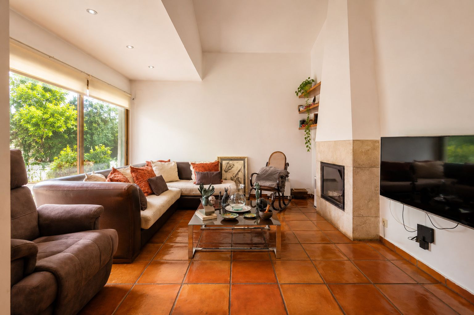 Luminoso salón con suelos de barro artesanal, chimenea revestida de piedra y amplios ventanales con vistas a la vegetación exterior. Luminoso salón con suelos de barro artesanal, chimenea revestida de piedra y amplios ventanales con vistas a la vegetación exterior.