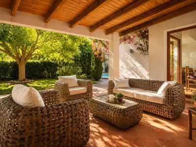 Amplia naya cubierta con techo de vigas de madera y suelo de barro, equipada con mobiliario trenzado y acceso directo al exuberante jardín y la piscina.