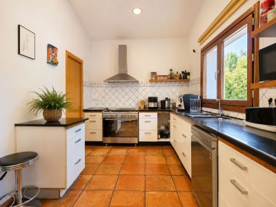 Cocina funcional con suelos de barro artesanal, encimeras oscuras y amplios ventanales de madera que aportan abundante luz natural.