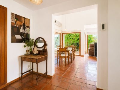 El luminoso recibidor, con suelo de barro artesanal y consola vintage, se abre a un amplio comedor con grandes ventanales que ofrecen vistas al exuberante jardín.