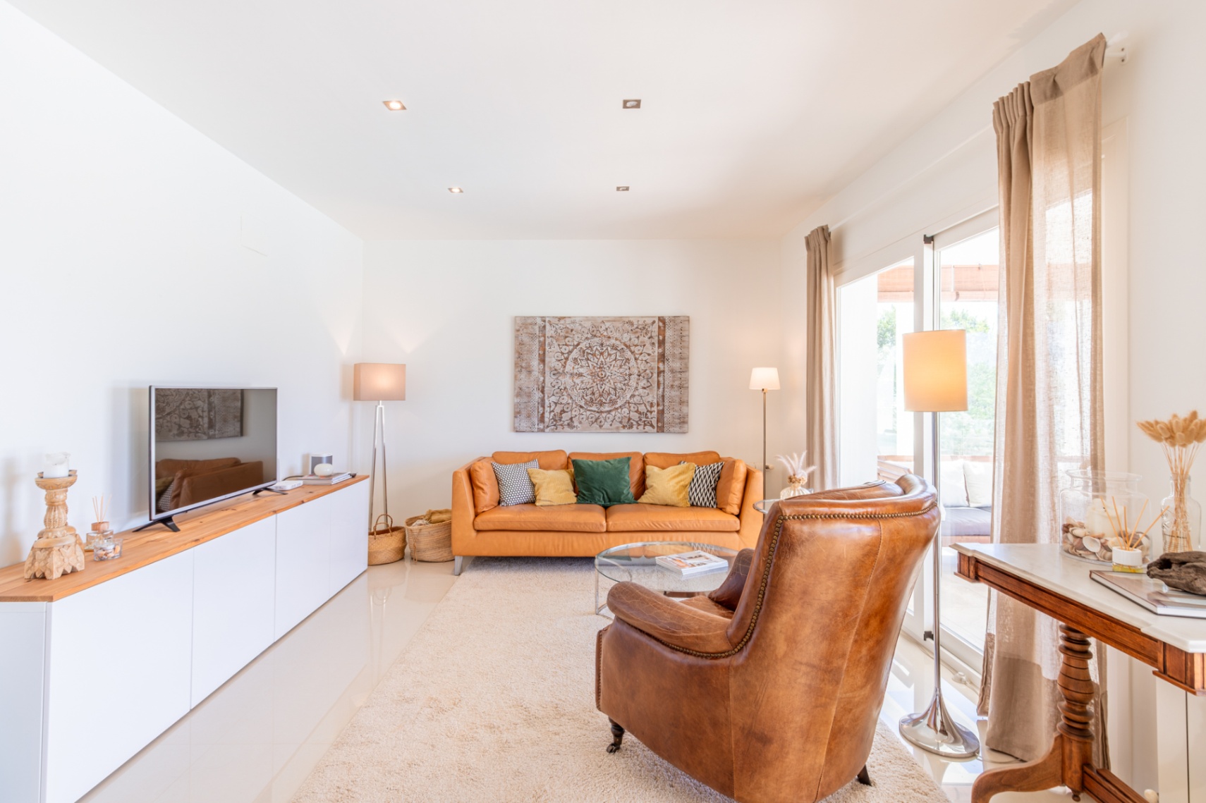 Amplio salón con sofá de cuero naranja, sillón individual y mueble de TV. La luz natural entra por las puertas correderas que dan a la terraza. Amplio salón con sofá de cuero naranja, sillón individual y mueble de TV. La luz natural entra por las puertas correderas que dan a la terraza.