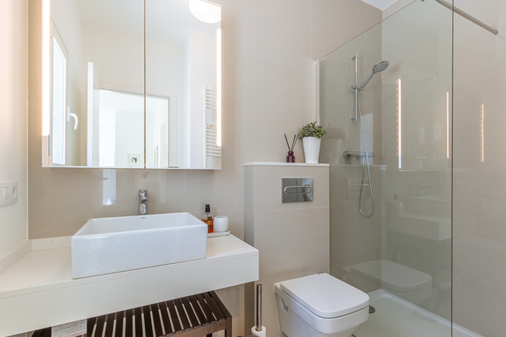Baño moderno con lavabo rectangular sobre encimera flotante, espejo con iluminación LED integrada y ducha acristalada. Paredes revestidas en tonos neutros. Baño moderno con lavabo rectangular sobre encimera flotante, espejo con iluminación LED integrada y ducha acristalada. Paredes revestidas en tonos neutros.