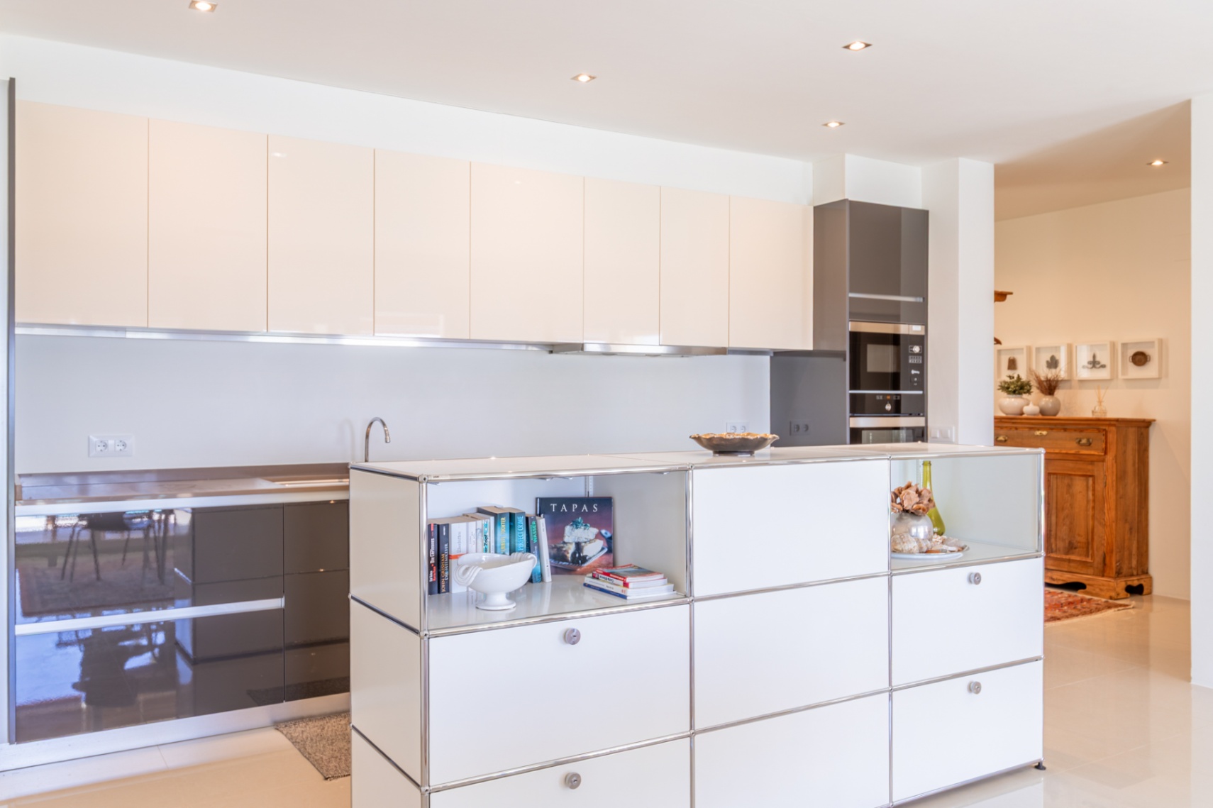 Cocina moderna con armarios superiores lacados en beige claro y bajos en gris oscuro. Isla central con estantes abiertos y electrodomésticos integrados. Cocina moderna con armarios superiores lacados en beige claro y bajos en gris oscuro. Isla central con estantes abiertos y electrodomésticos integrados.