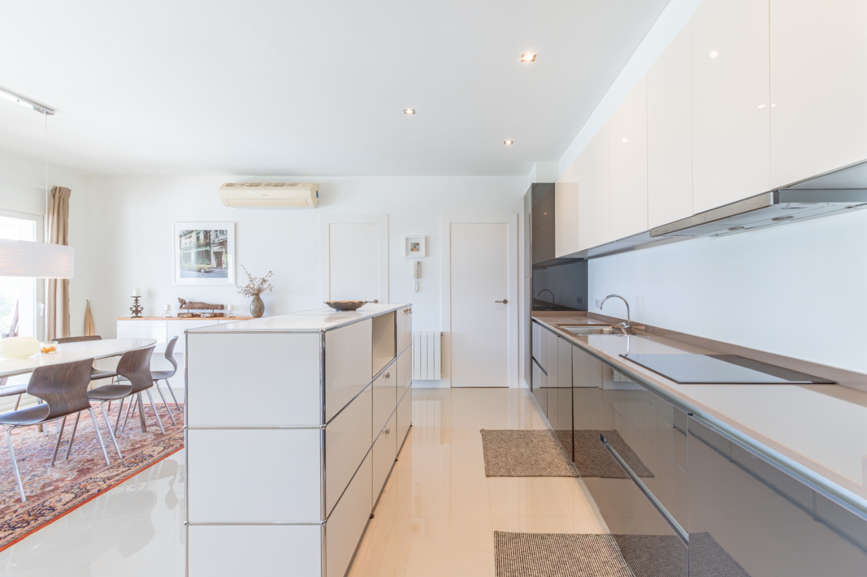 Cocina moderna de concepto abierto con armarios blancos y grises brillantes, placa de inducción integrada y una isla modular. Comedor adyacente con mesa ovalada y sillas de madera. Cocina moderna de concepto abierto con armarios blancos y grises brillantes, placa de inducción integrada y una isla modular. Comedor adyacente con mesa ovalada y sillas de madera.
