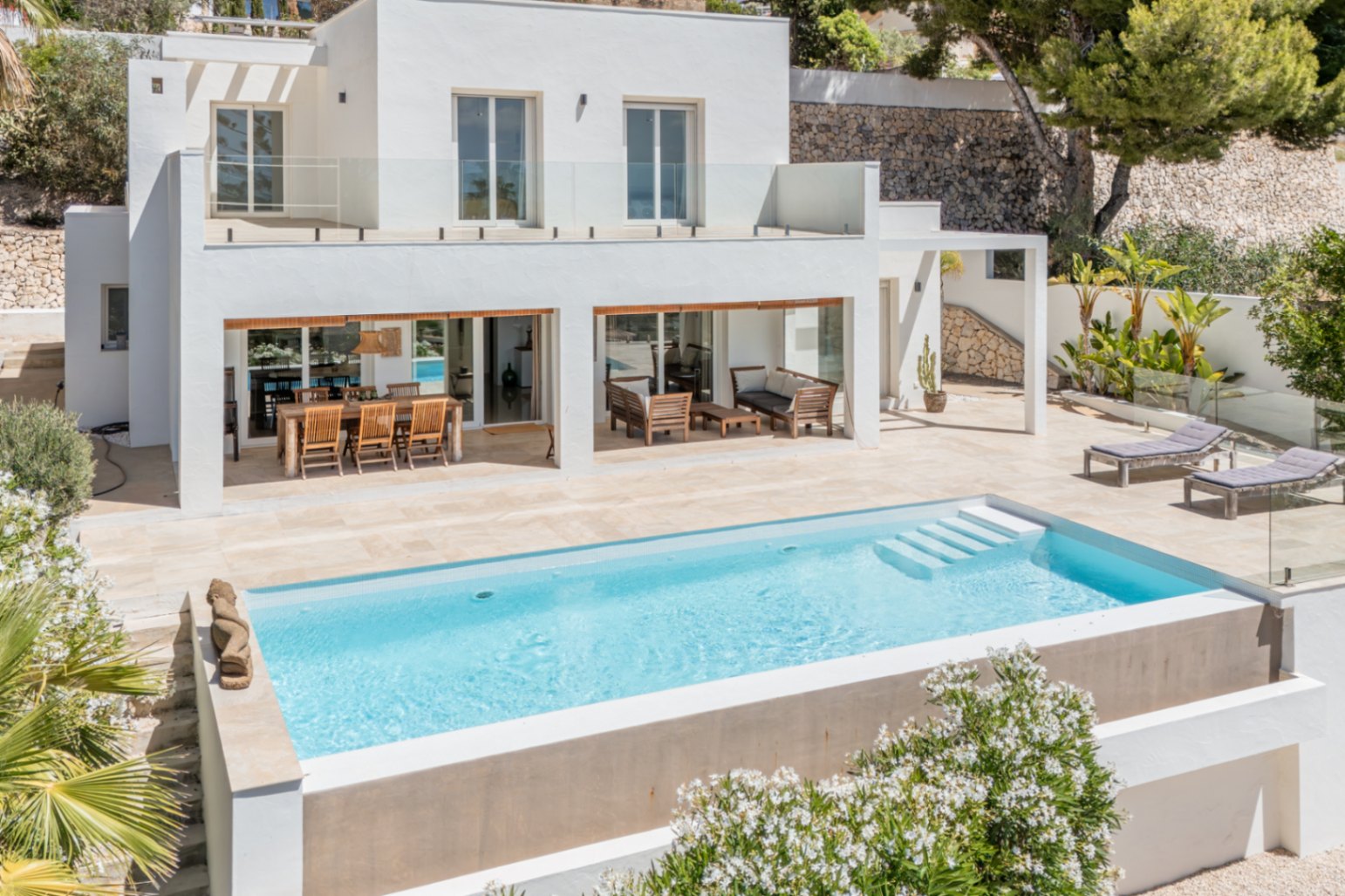 La villa moderna exhibe una piscina rectangular con escalones y una amplia terraza de piedra clara. Incluye zona de comedor exterior y salón, con balcón superior de barandilla de cristal. La villa moderna exhibe una piscina rectangular con escalones y una amplia terraza de piedra clara. Incluye zona de comedor exterior y salón, con balcón superior de barandilla de cristal.