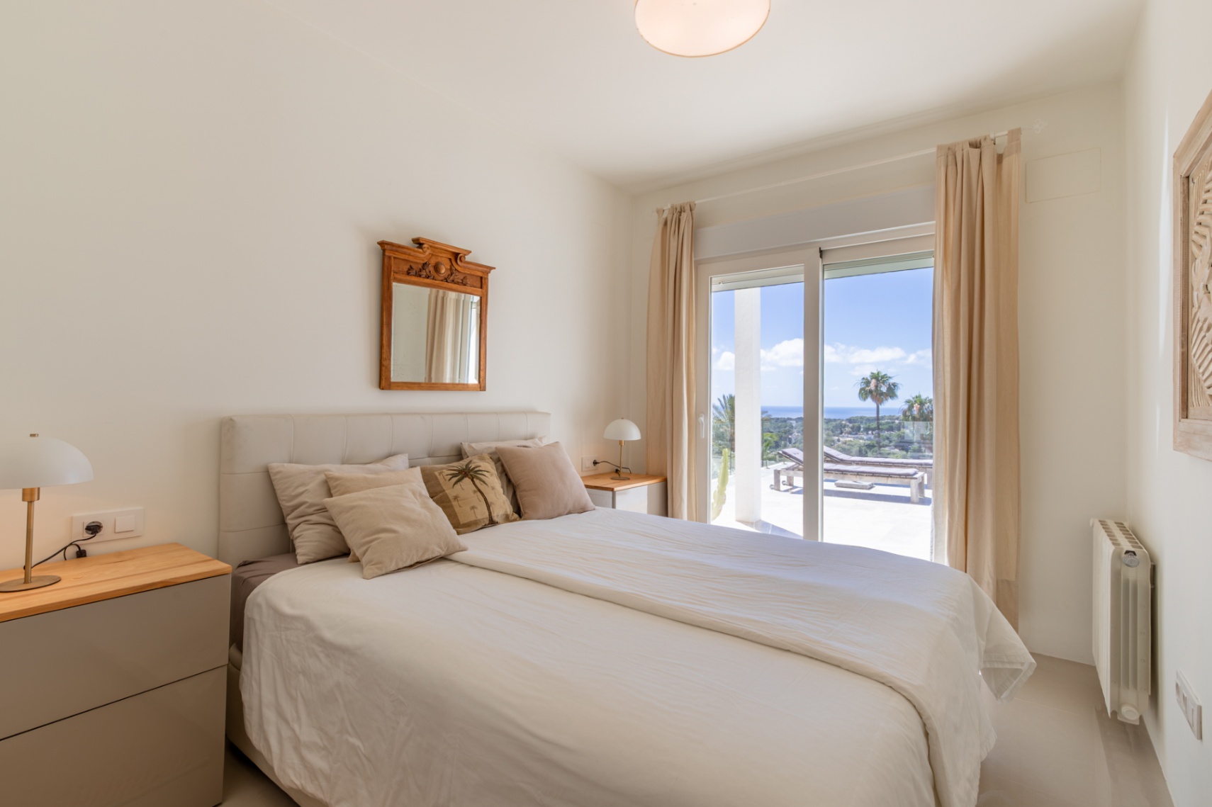 Luminoso dormitorio con cama, mesitas de noche y acceso directo a una terraza con tumbonas y vistas panorámicas al mar. Luminoso dormitorio con cama, mesitas de noche y acceso directo a una terraza con tumbonas y vistas panorámicas al mar.