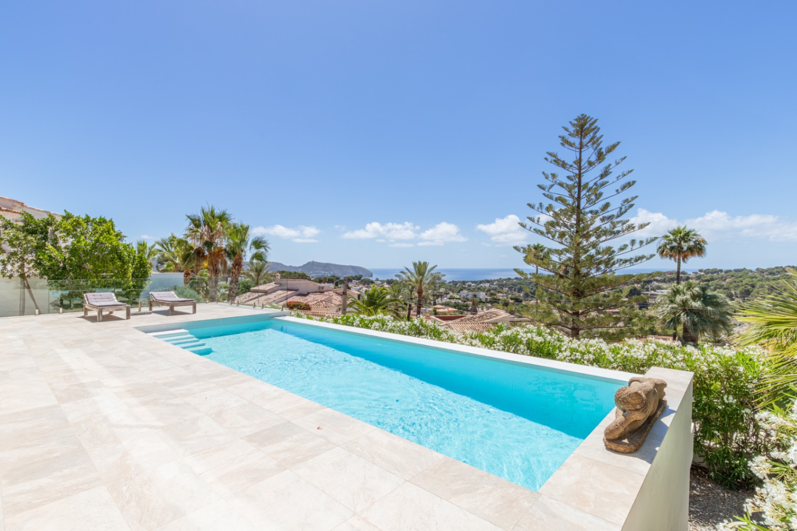 Piscina infinita con baldosas claras y terraza de gres, ofreciendo vistas panorámicas ininterrumpidas al Mediterráneo. Dos tumbonas y exuberante vegetación costera completan el exterior. Piscina infinita con baldosas claras y terraza de gres, ofreciendo vistas panorámicas ininterrumpidas al Mediterráneo. Dos tumbonas y exuberante vegetación costera completan el exterior.