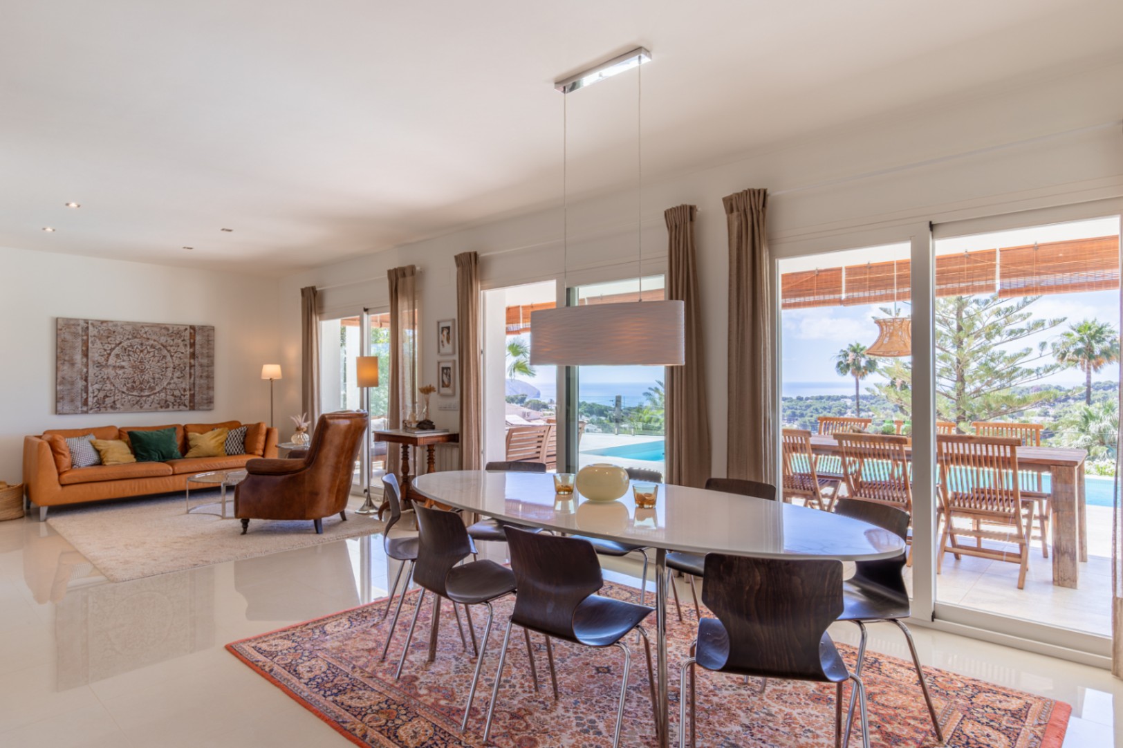 Salón-comedor de concepto abierto con mesa ovalada, sofá naranja y vistas panorámicas al Mediterráneo desde sus amplios ventanales. Salón-comedor de concepto abierto con mesa ovalada, sofá naranja y vistas panorámicas al Mediterráneo desde sus amplios ventanales.