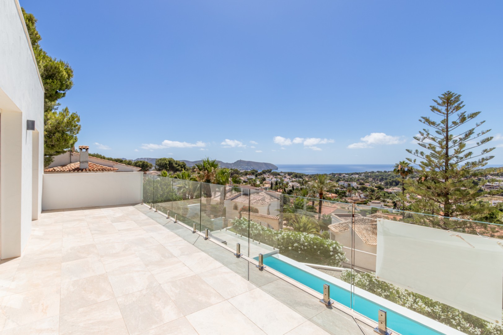 Terraza exterior con suelo de gres claro y barandilla de cristal. Vistas panorámicas al mar Mediterráneo, la bahía y el entorno urbano, incluyendo una piscina alargada y vegetación. Terraza exterior con suelo de gres claro y barandilla de cristal. Vistas panorámicas al mar Mediterráneo, la bahía y el entorno urbano, incluyendo una piscina alargada y vegetación.