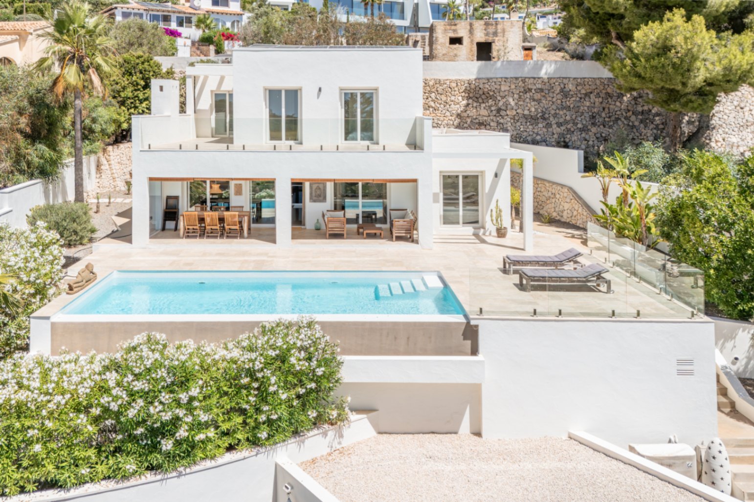 Villa moderna de dos plantas con piscina rectangular y amplia terraza solada. Destacan la zona de comedor exterior cubierta y la barandilla de cristal, integrando el diseño con el entorno mediterráneo. Villa moderna de dos plantas con piscina rectangular y amplia terraza solada. Destacan la zona de comedor exterior cubierta y la barandilla de cristal, integrando el diseño con el entorno mediterráneo.