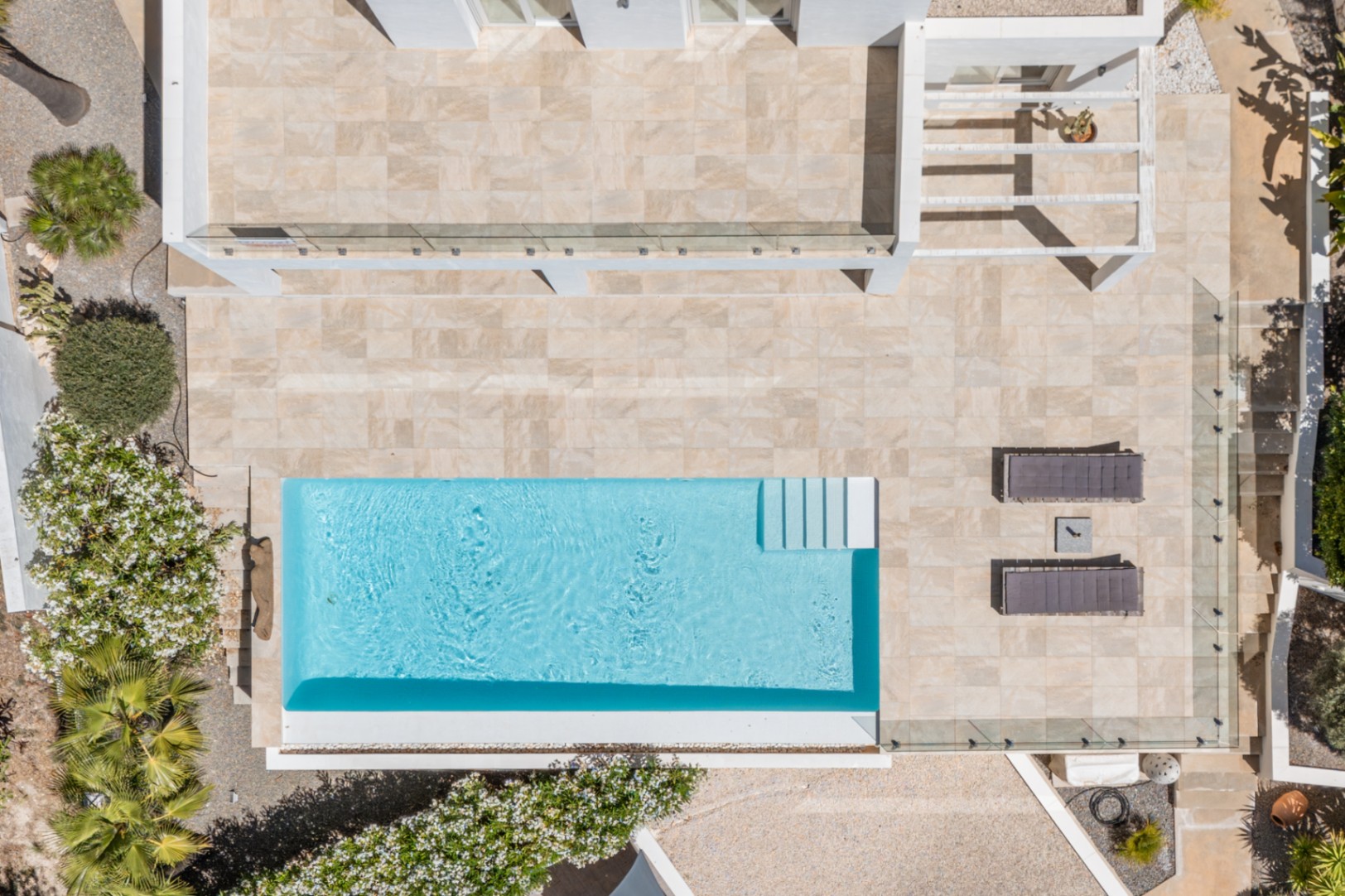 Vista aérea de la piscina rectangular de agua azul, rodeada por una amplia terraza de baldosas claras, con tumbonas y vegetación mediterránea. Vista aérea de la piscina rectangular de agua azul, rodeada por una amplia terraza de baldosas claras, con tumbonas y vegetación mediterránea.
