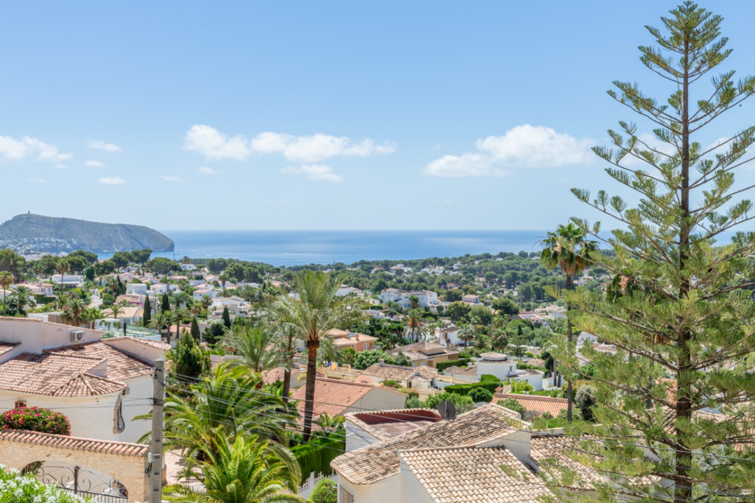 Vista elevada de la costa mediterránea, mostrando tejados de teja, exuberante vegetación y un promontorio rocoso que se adentra en el mar azul bajo un cielo despejado. Vista elevada de la costa mediterránea, mostrando tejados de teja, exuberante vegetación y un promontorio rocoso que se adentra en el mar azul bajo un cielo despejado.