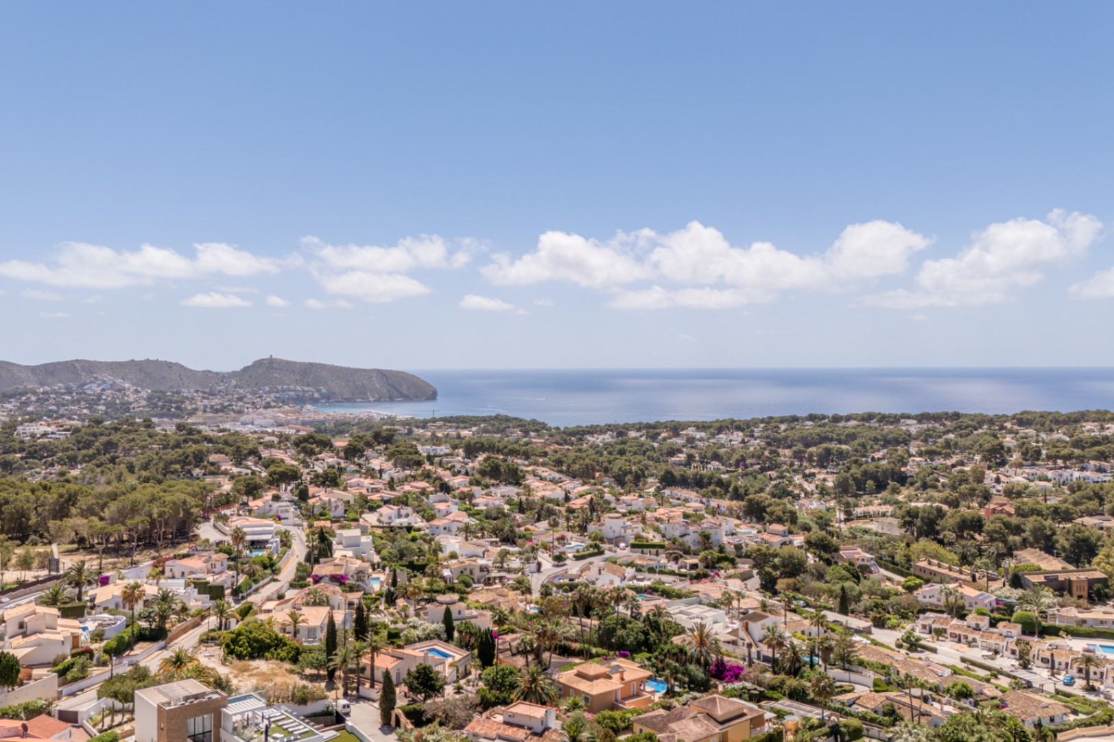 Vista panorámica de una zona residencial costera, con tejados de terracota, abundante vegetación y el mar Mediterráneo extendiéndose hasta el horizonte. Vista panorámica de una zona residencial costera, con tejados de terracota, abundante vegetación y el mar Mediterráneo extendiéndose hasta el horizonte.