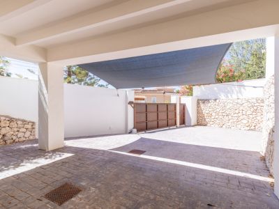 Amplio aparcamiento privado con pavimento texturizado, toldo protector y portón metálico corredero, enmarcado por muros blancos y de piedra natural.
