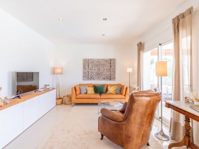 Amplio salón con sofá de cuero naranja, sillón individual y mueble de TV. La luz natural entra por las puertas correderas que dan a la terraza.