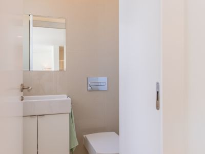 Aseo de cortesía moderno con lavabo blanco sobre mueble, espejo, inodoro suspendido y paredes de azulejos beige. Diseño funcional y limpio.