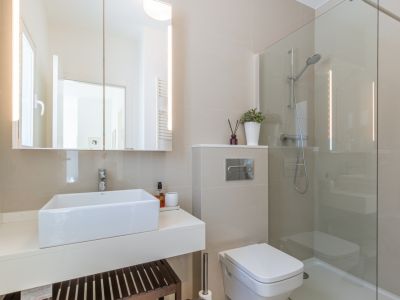 Baño moderno con lavabo rectangular sobre encimera flotante, espejo con iluminación LED integrada y ducha acristalada. Paredes revestidas en tonos neutros.