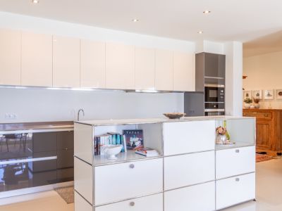 Cocina moderna con armarios superiores lacados en beige claro y bajos en gris oscuro. Isla central con estantes abiertos y electrodomésticos integrados.