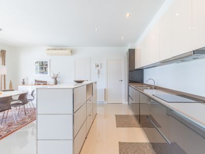 Cocina moderna de concepto abierto con armarios blancos y grises brillantes, placa de inducción integrada y una isla modular. Comedor adyacente con mesa ovalada y sillas de madera.