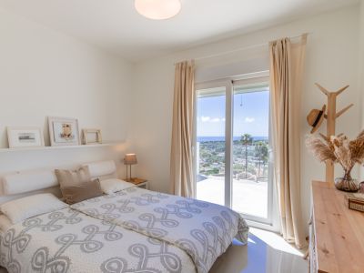 Dormitorio luminoso en planta alta con acceso a terraza, ofreciendo vistas panorámicas al mar Mediterráneo. Incluye mobiliario de madera clara y suelos de azulejo.