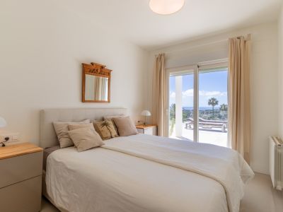 Luminoso dormitorio con cama, mesitas de noche y acceso directo a una terraza con tumbonas y vistas panorámicas al mar.